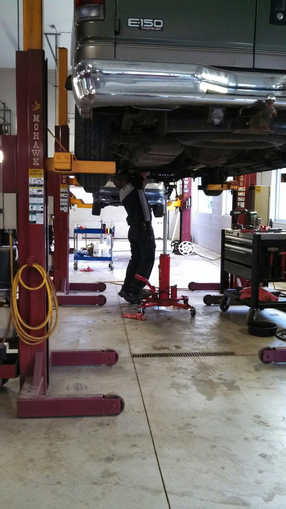 Person working under a lifted green car in an auto repair shop