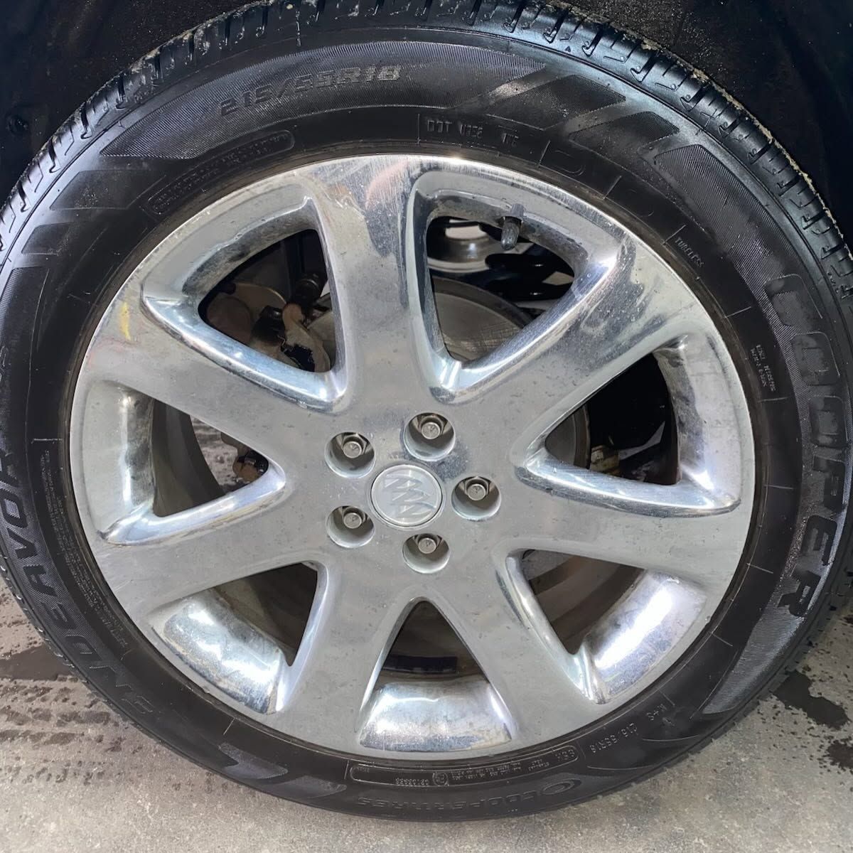 Silver car wheel with a worn tire and five spokes on pavement