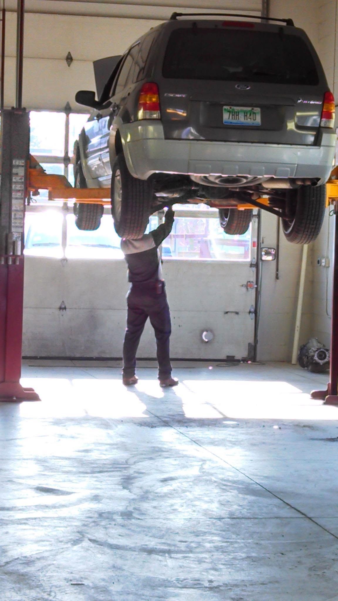 Mechanic working under a raised silver SUV in an auto repair shop