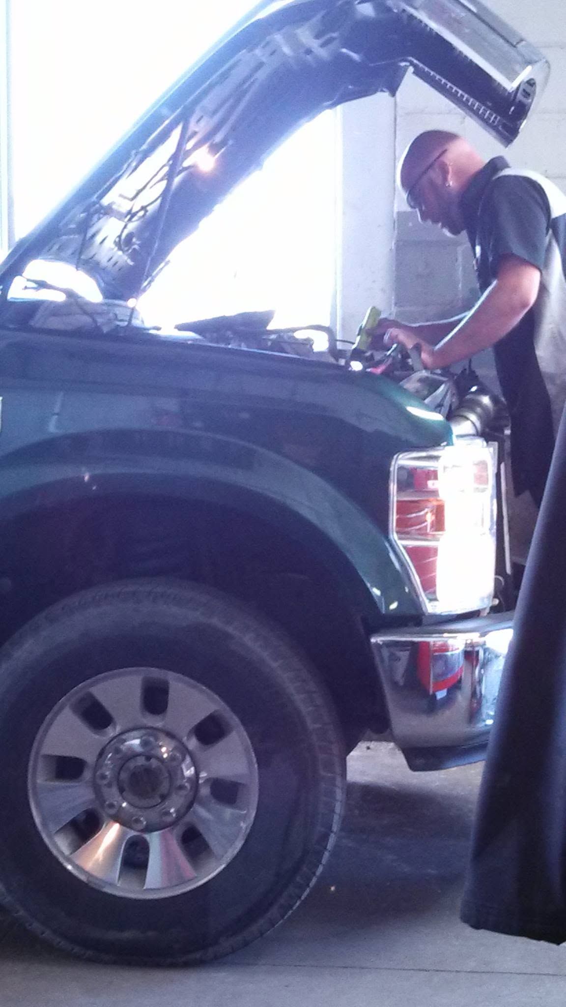 Person inspecting a black SUV with hood open in a driveway, holding tools near the engine