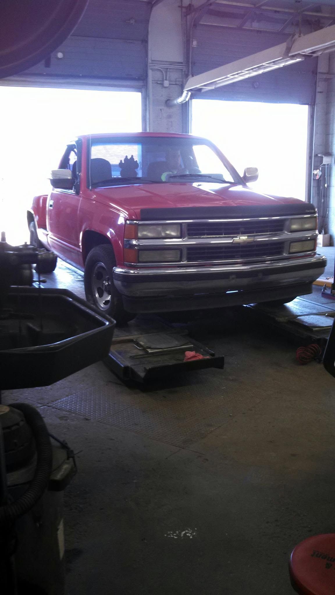 Red pickup truck on a lift inside an auto garage, front view.