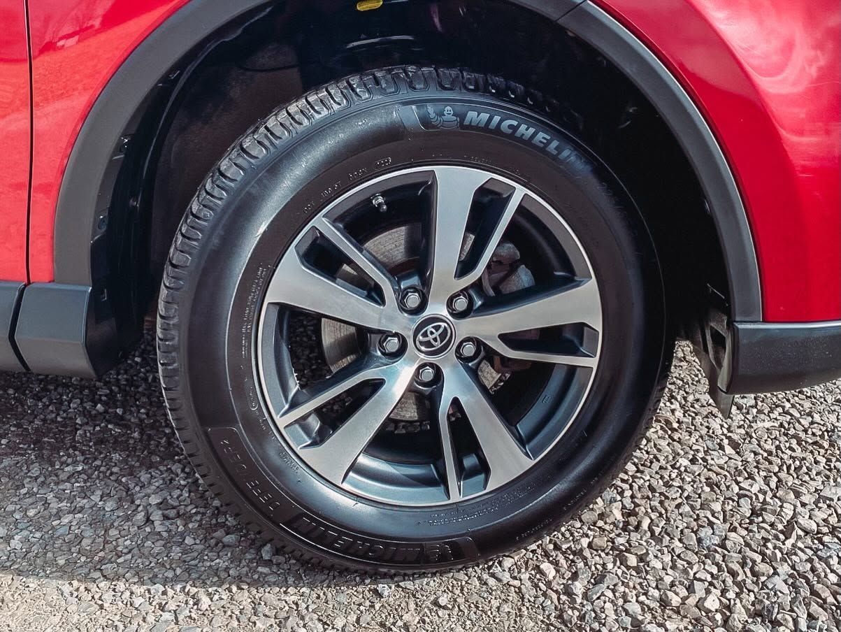 Close-up of a red car’s rear wheel with a black tire and silver alloy rim.