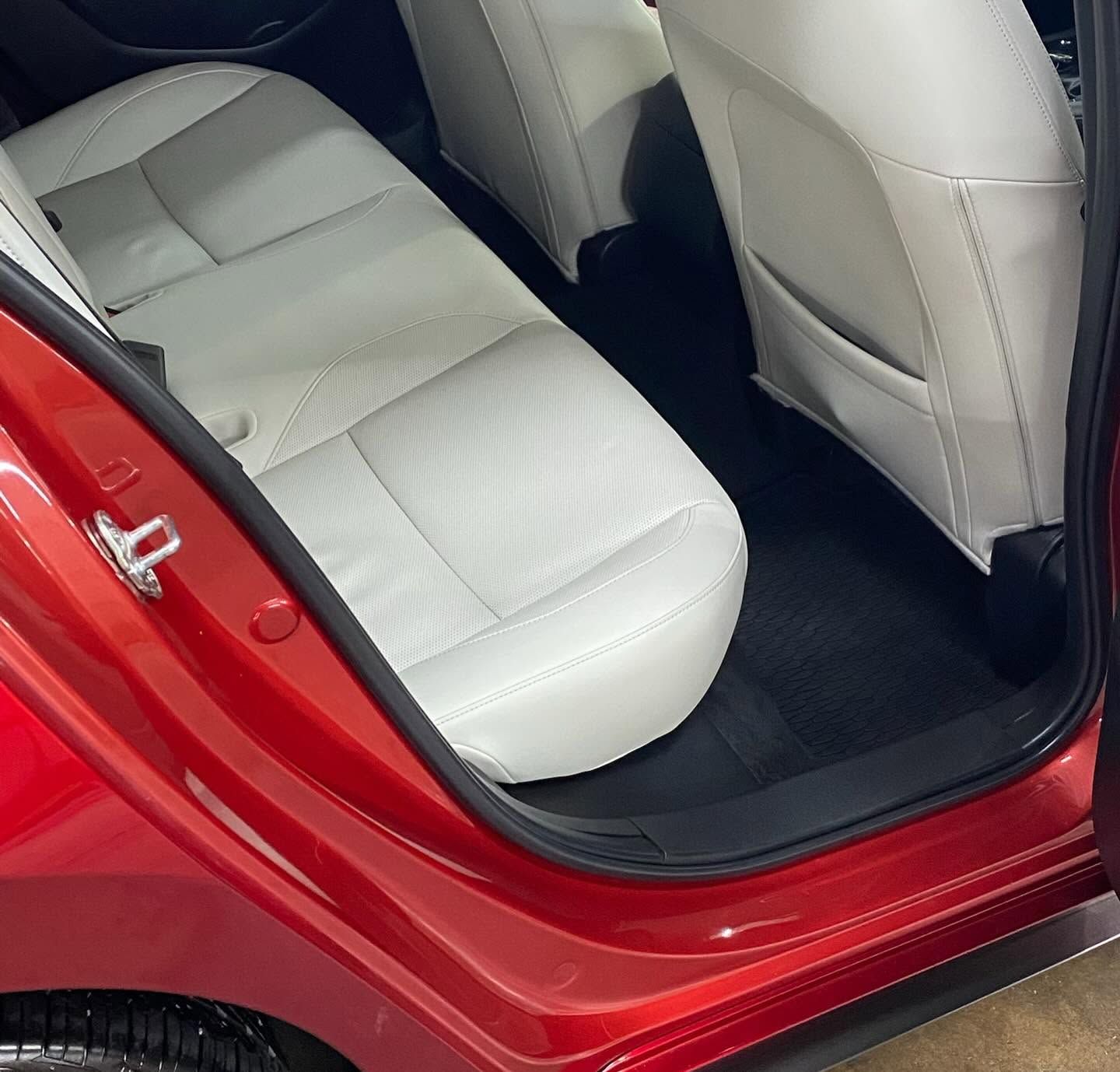 Open red car door revealing white leather rear seats and black floor mats