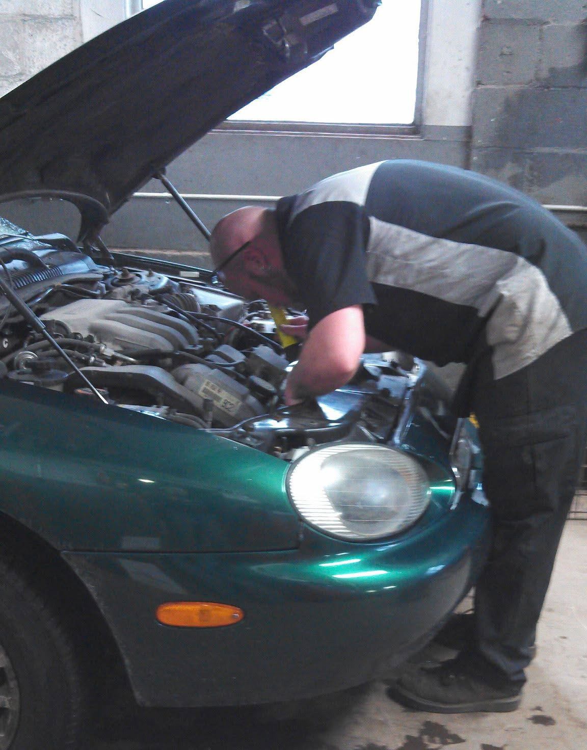 Person working under the hood of a green car in a garage