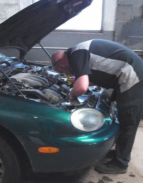 Person working under the hood of a green car in a garage
