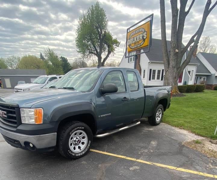 Gray GMC pickup parked outside a dealership sign on a cloudy day