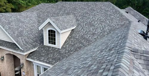 Gray shingled house roof with dormer windows and a brick exterior section
