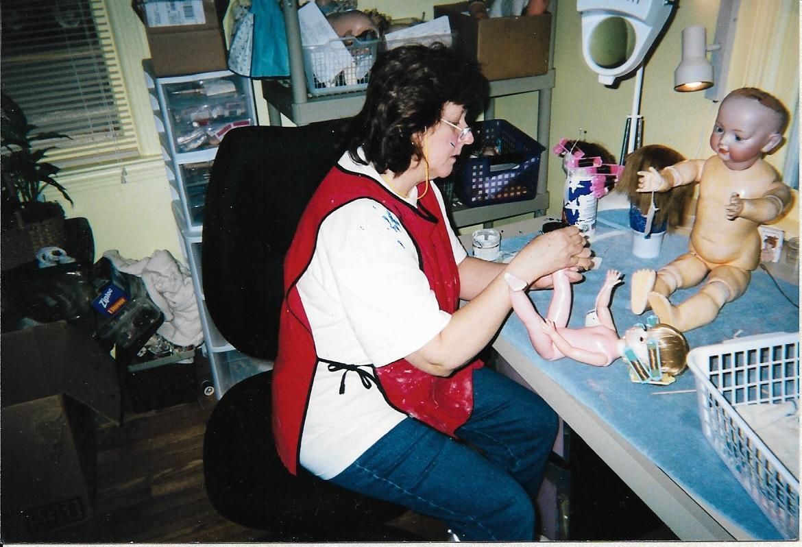 A person in a lab coat examines a doll with paintbrushes nearby.