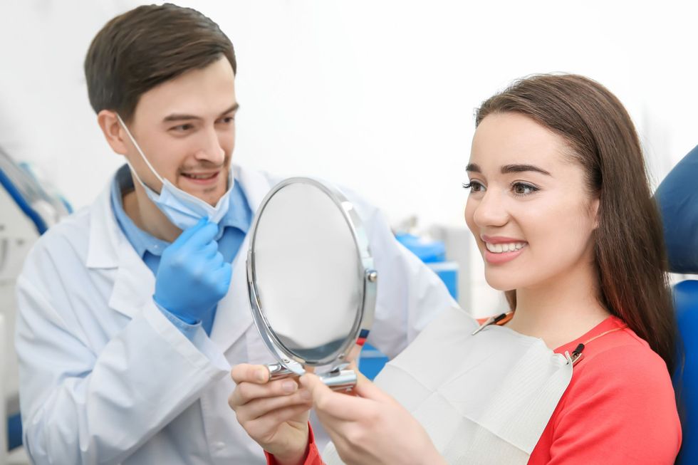 Dentist showing a mirror to a smiling patient in a clinic, wearing a mask and blue gloves