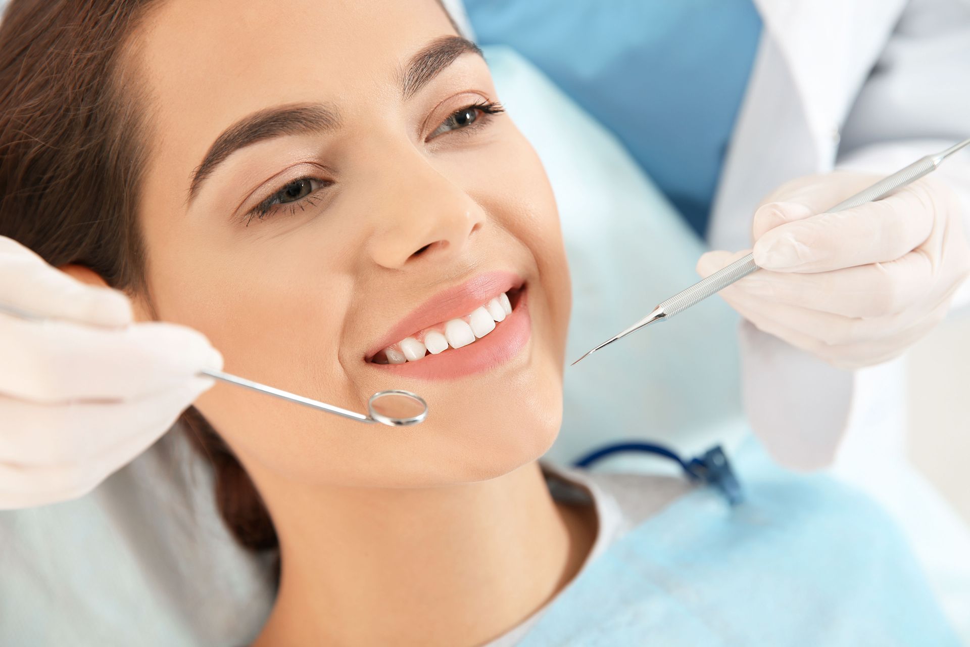 Dentist examining a smiling patient’s teeth with mirror and probe