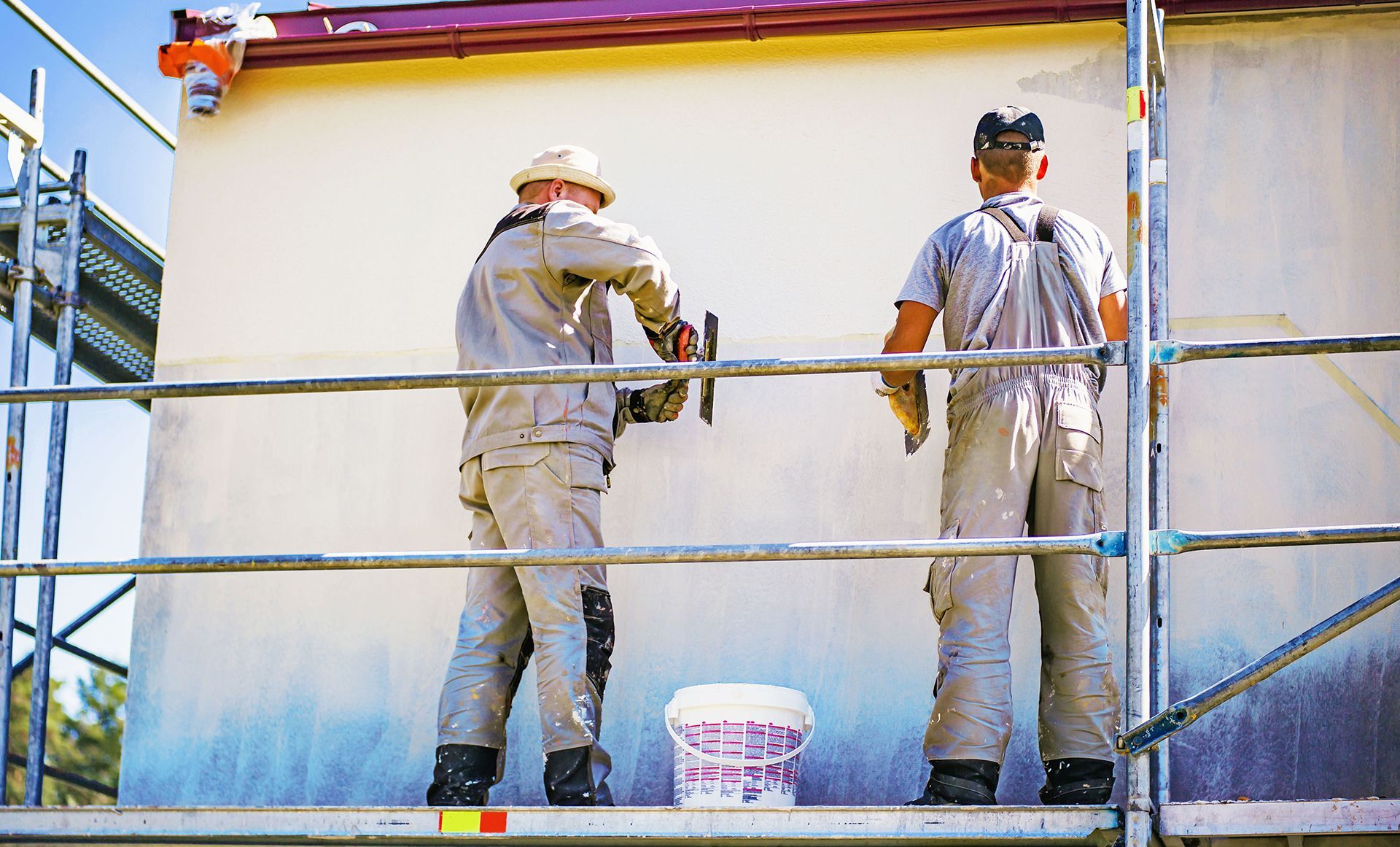 Two men are standing on a scaffolding painting a building.