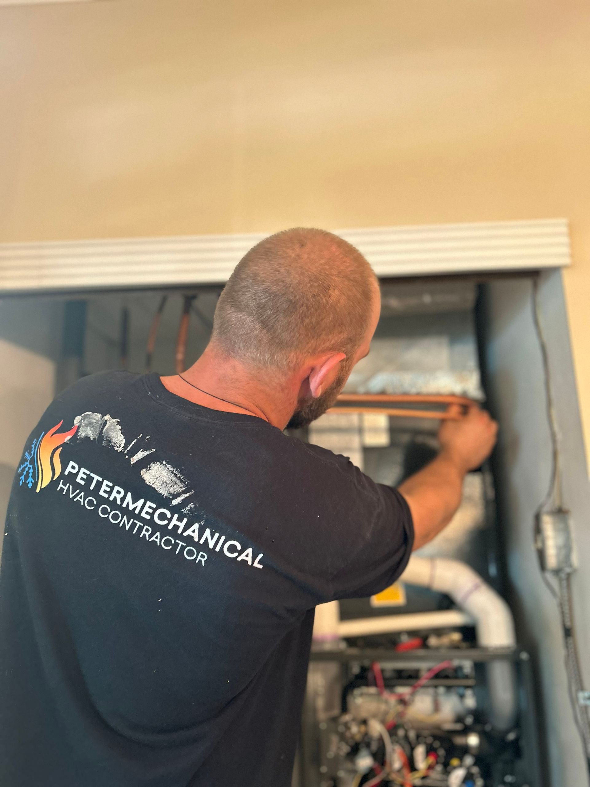 Technician working inside an HVAC unit, reaching toward equipment with tools.