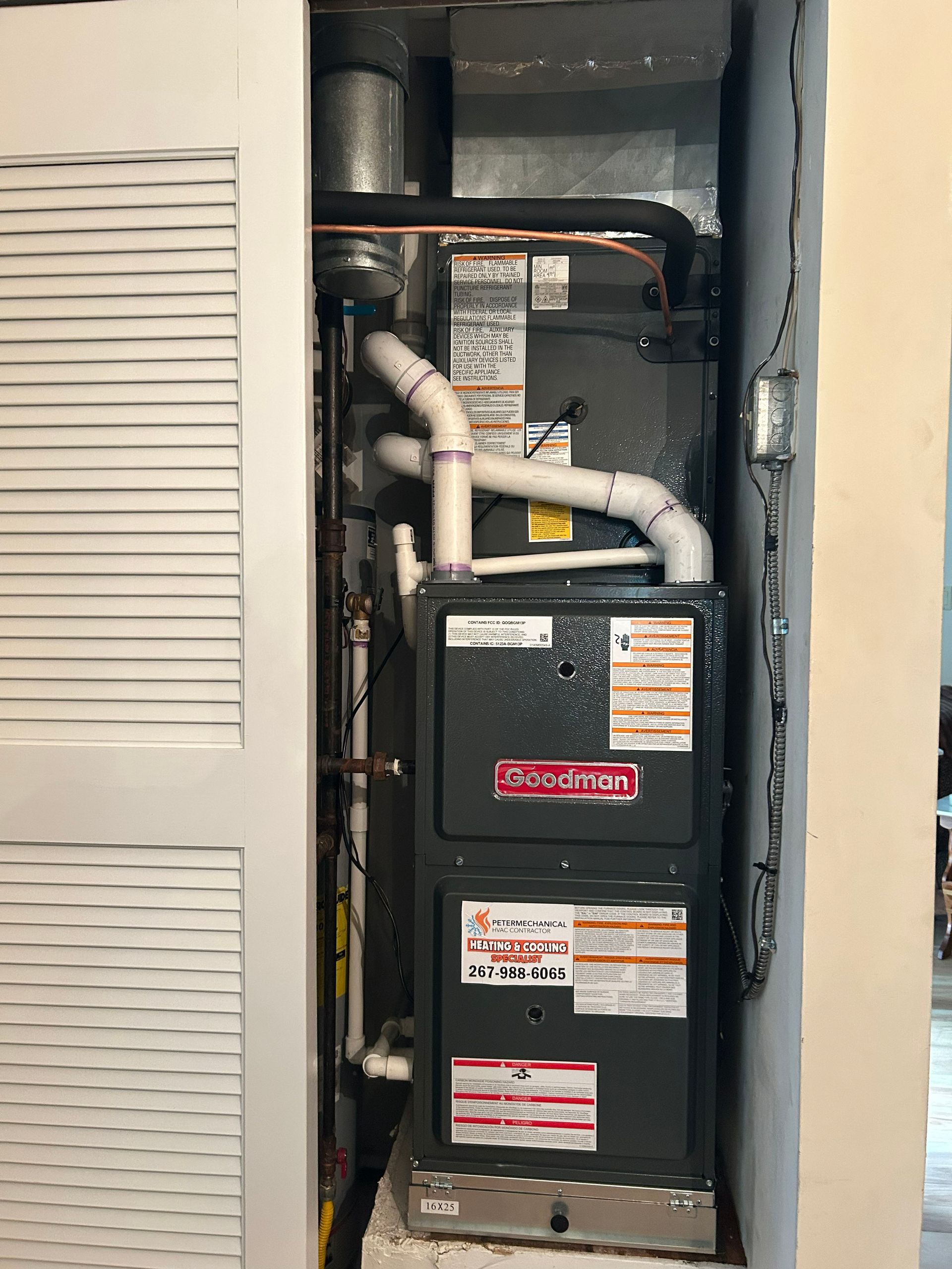 Open HVAC furnace and ductwork in a narrow utility closet, with white pipes and black equipment.