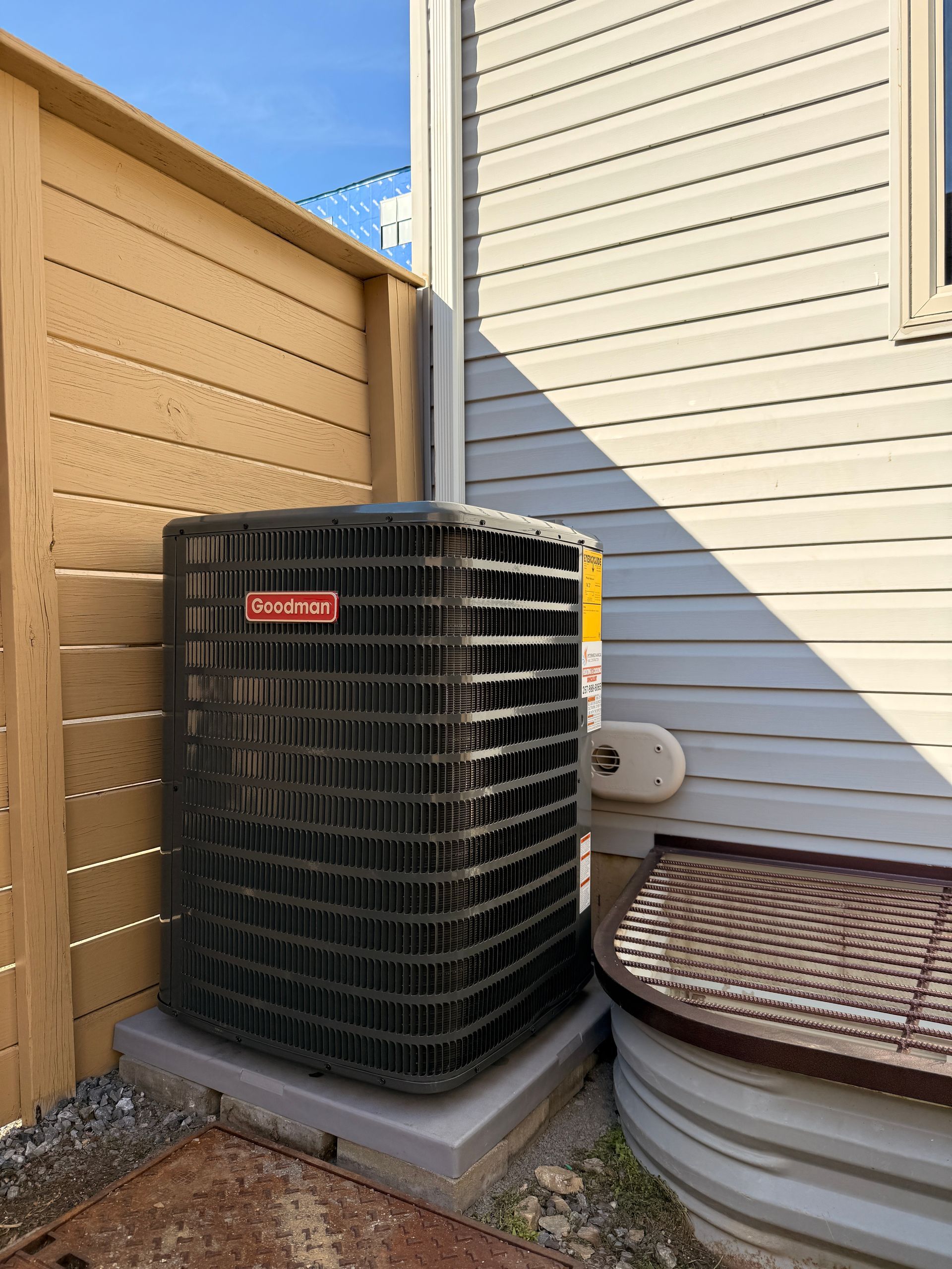 Outdoor HVAC unit beside a beige house and wooden fence, with a covered hot tub nearby.