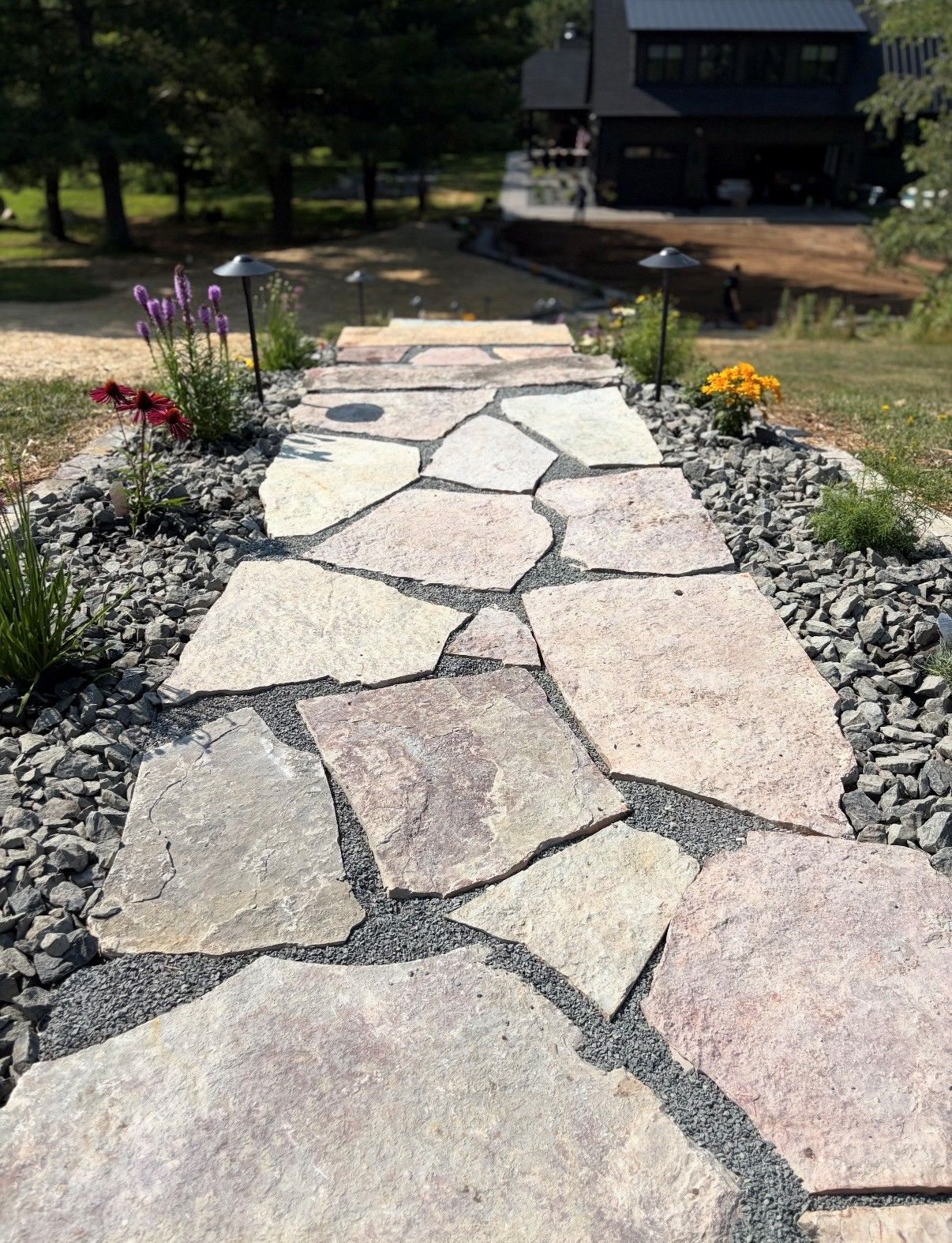 Stone garden path leading to a house, bordered by gray rocks and small flowers.