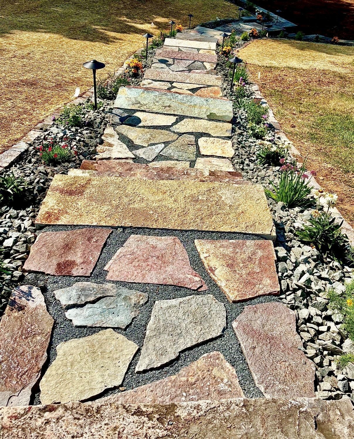 Stone walkway with irregular multicolored flagstones bordered by gravel and small plants in a yard