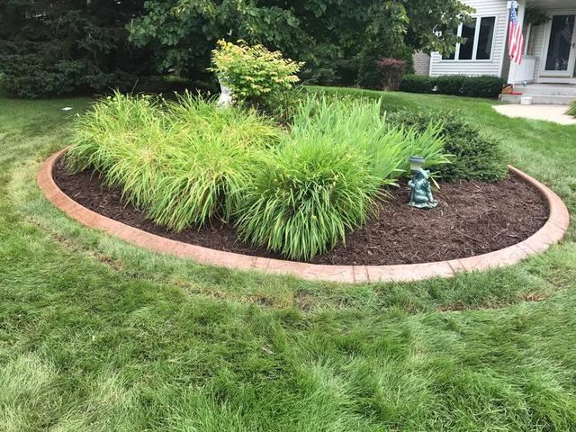 a circular garden in the middle of a lush green lawn in front of a house .
