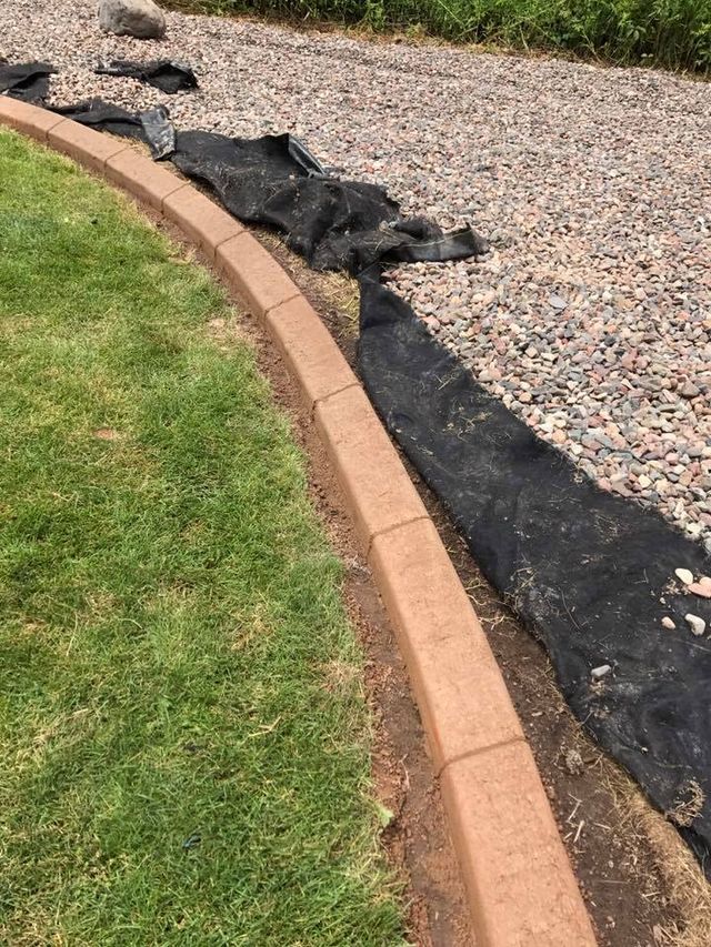 a brick curb is sitting on top of a lush green lawn next to a gravel driveway .