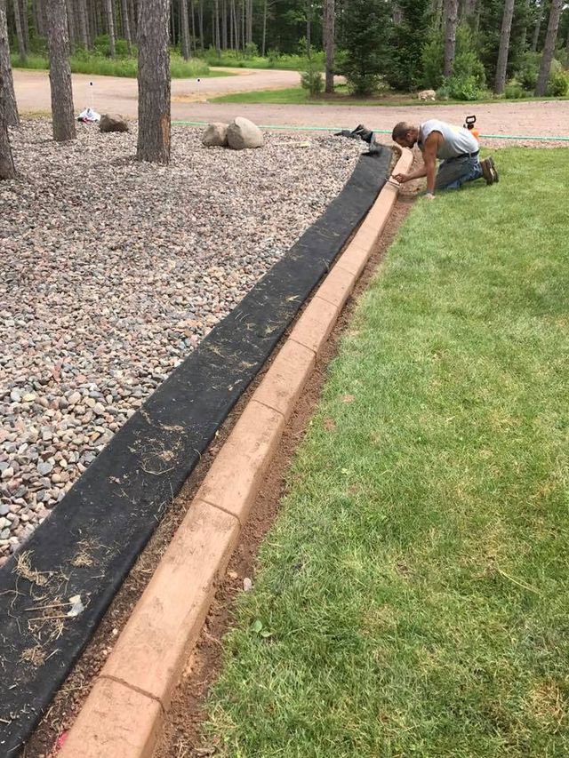 a man is kneeling down in the grass next to a concrete curb .