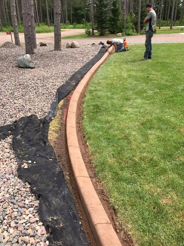 a man is kneeling on the grass next to a concrete curb .