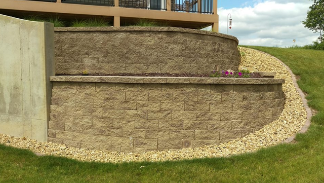 a brick wall is sitting on top of a grassy hill next to a house .