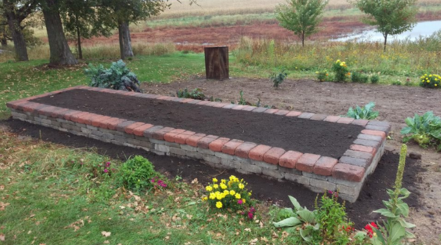 a brick planter filled with dirt and flowers in a garden .