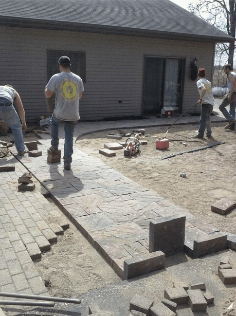 a group of men are working on a brick walkway in front of a house .