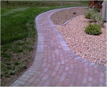 a brick walkway going through a lush green field