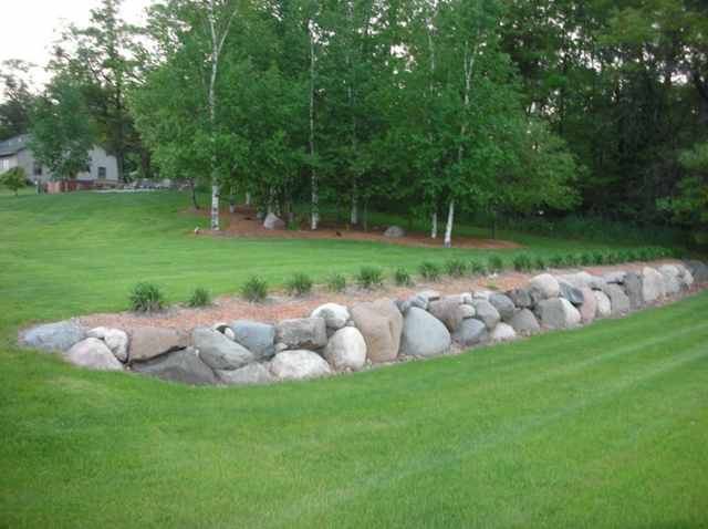 a large rock wall in the middle of a lush green field