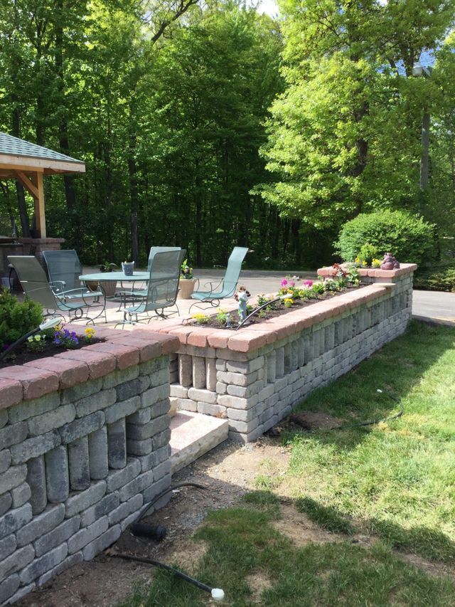 a brick wall surrounds a patio with a gazebo in the background .