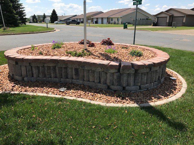 a brick wall with flowers in it is in the middle of a lush green field .