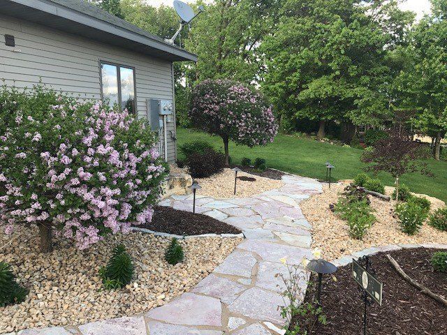 a stone walkway leading to a house surrounded by trees and bushes .