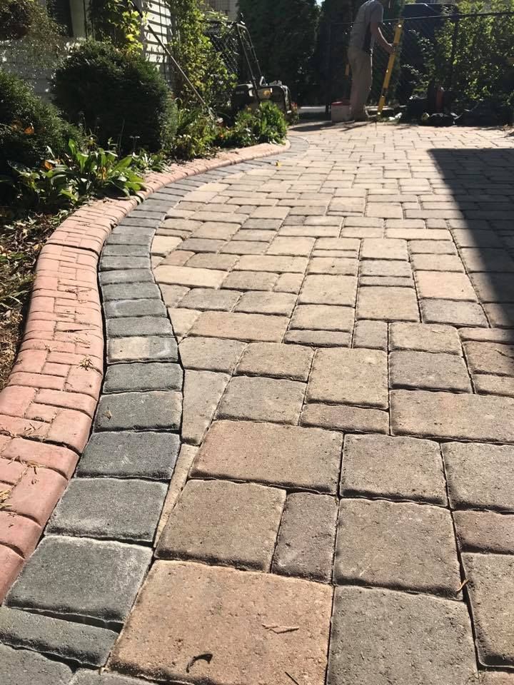 a brick walkway with a brick border and a man standing in the background .