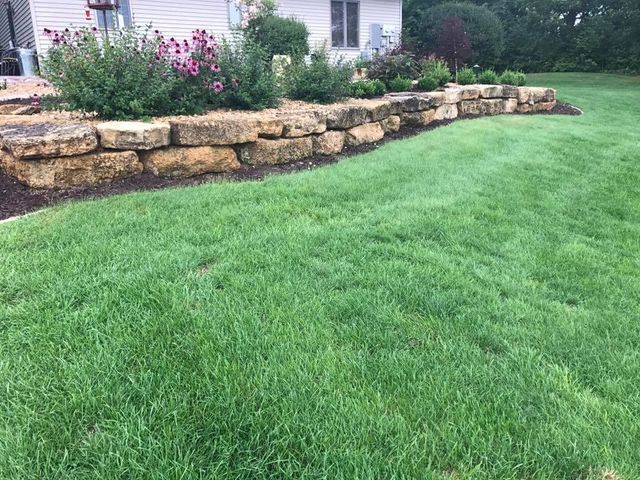 a lush green lawn in front of a house with a stone wall .