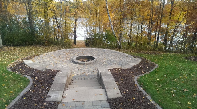 a fire pit in the middle of a lush green field next to a lake .