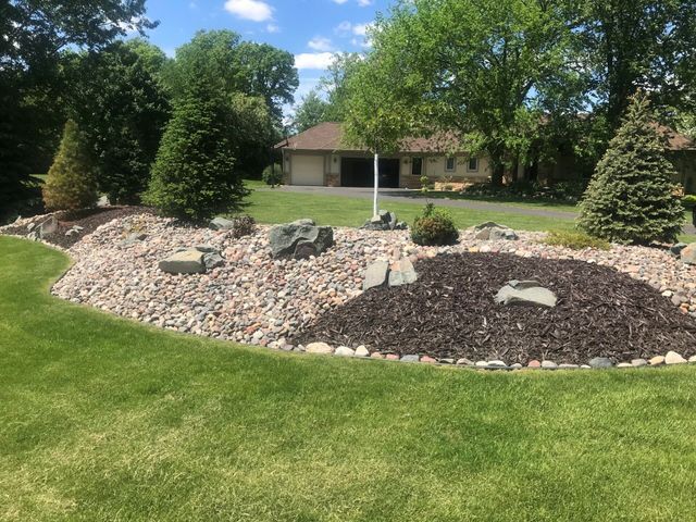 a lush green lawn with rocks and mulch in front of a house .