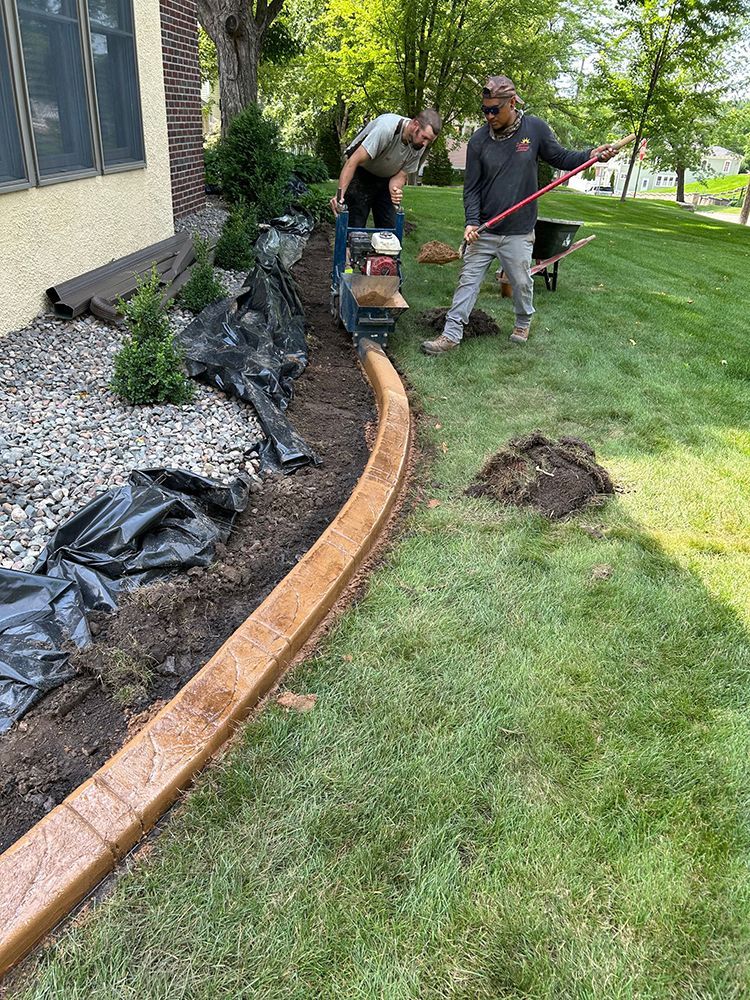 Two men are working on a concrete curb in a yard.