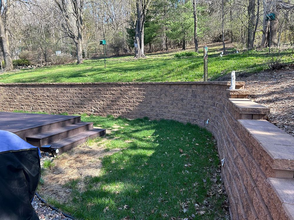 A brick wall surrounds a lush green field with trees in the background.