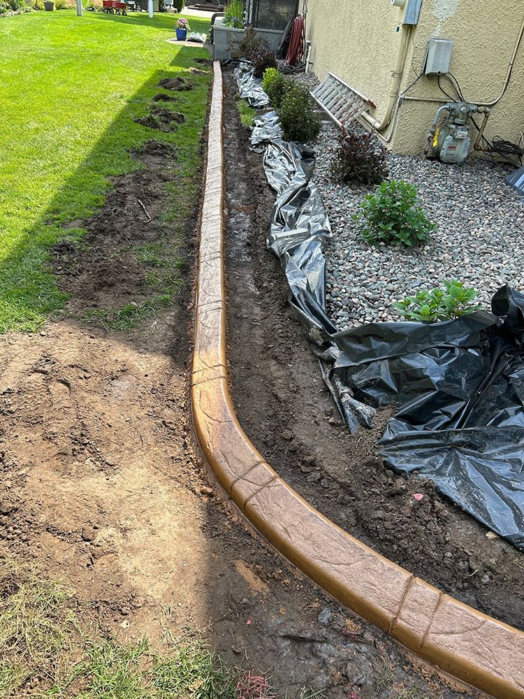 A concrete curb is being installed in a garden next to a house.