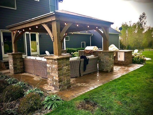 a patio with a wooden pavilion and a grill in the backyard of a house .