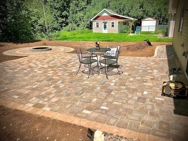 a patio with a table and chairs and a fire pit in the background .