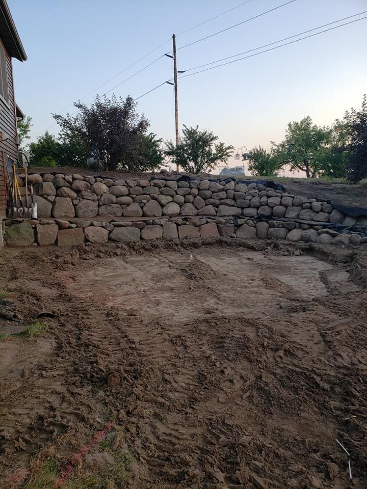 a large rock wall is being built in the dirt in front of a house .