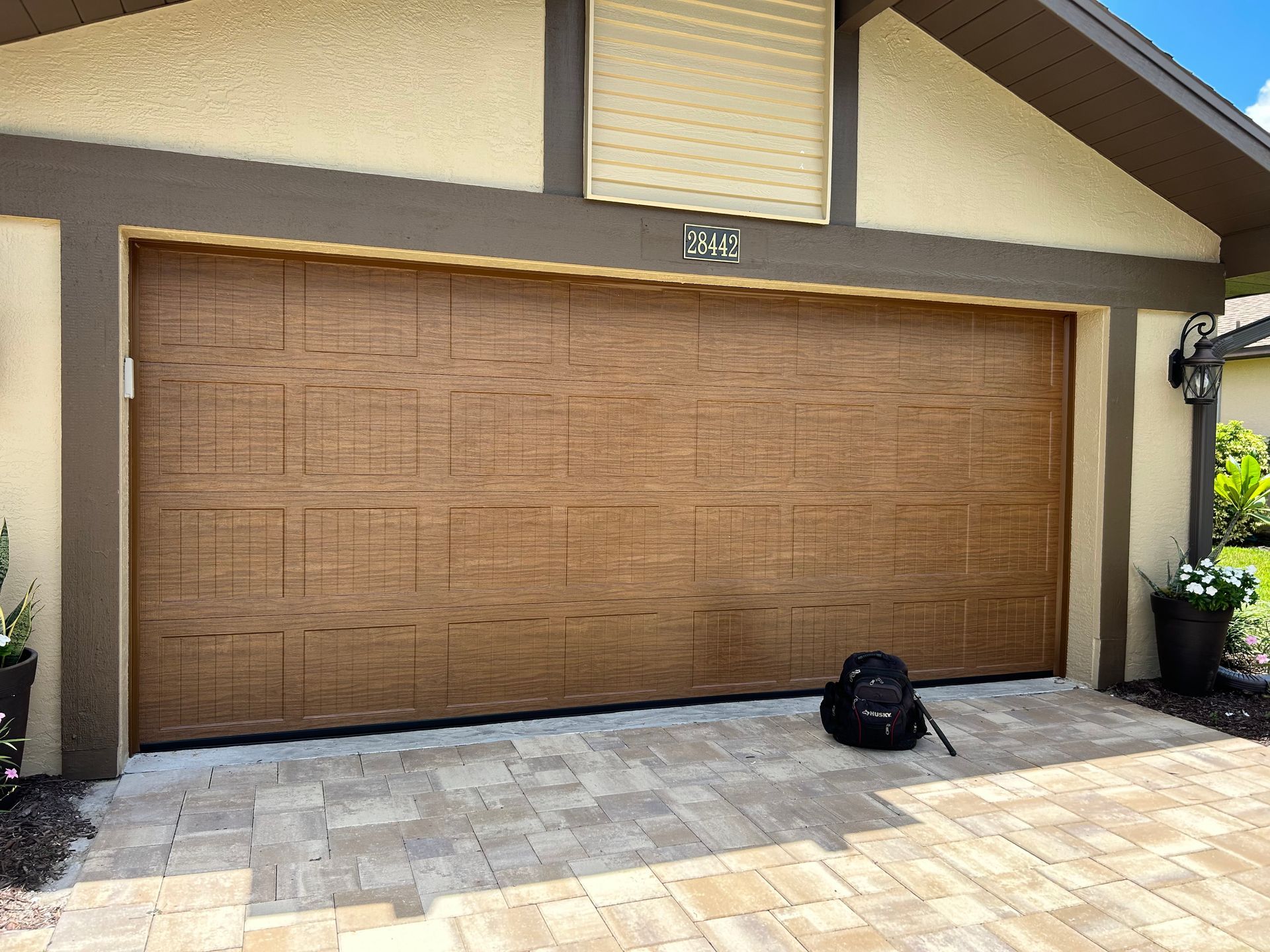 Two-car tan garage door on a beige house with a stone driveway and a black bag in front