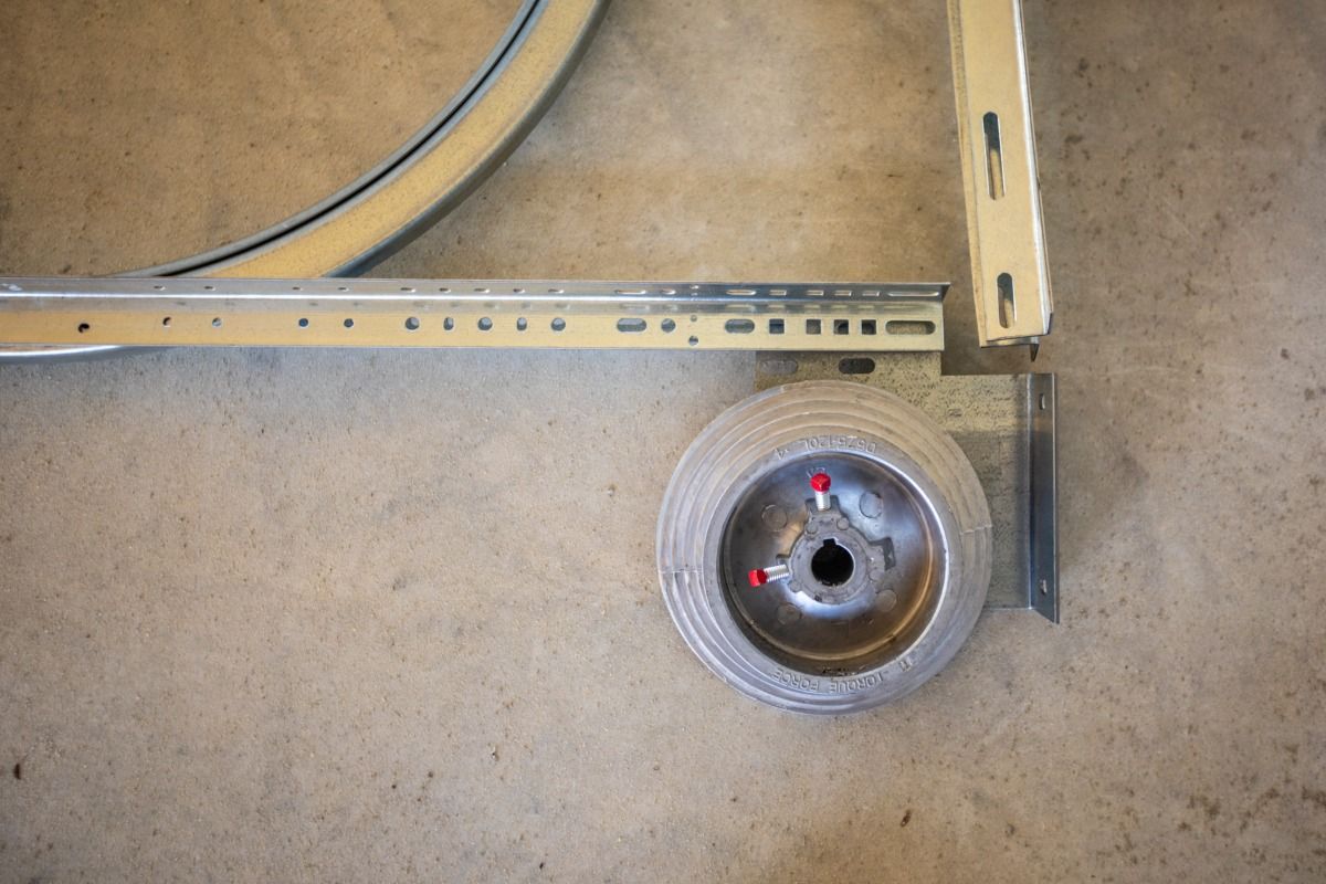 Garage door components: track, wheel, angle bracket, and curved metal piece, lying on a concrete floor.