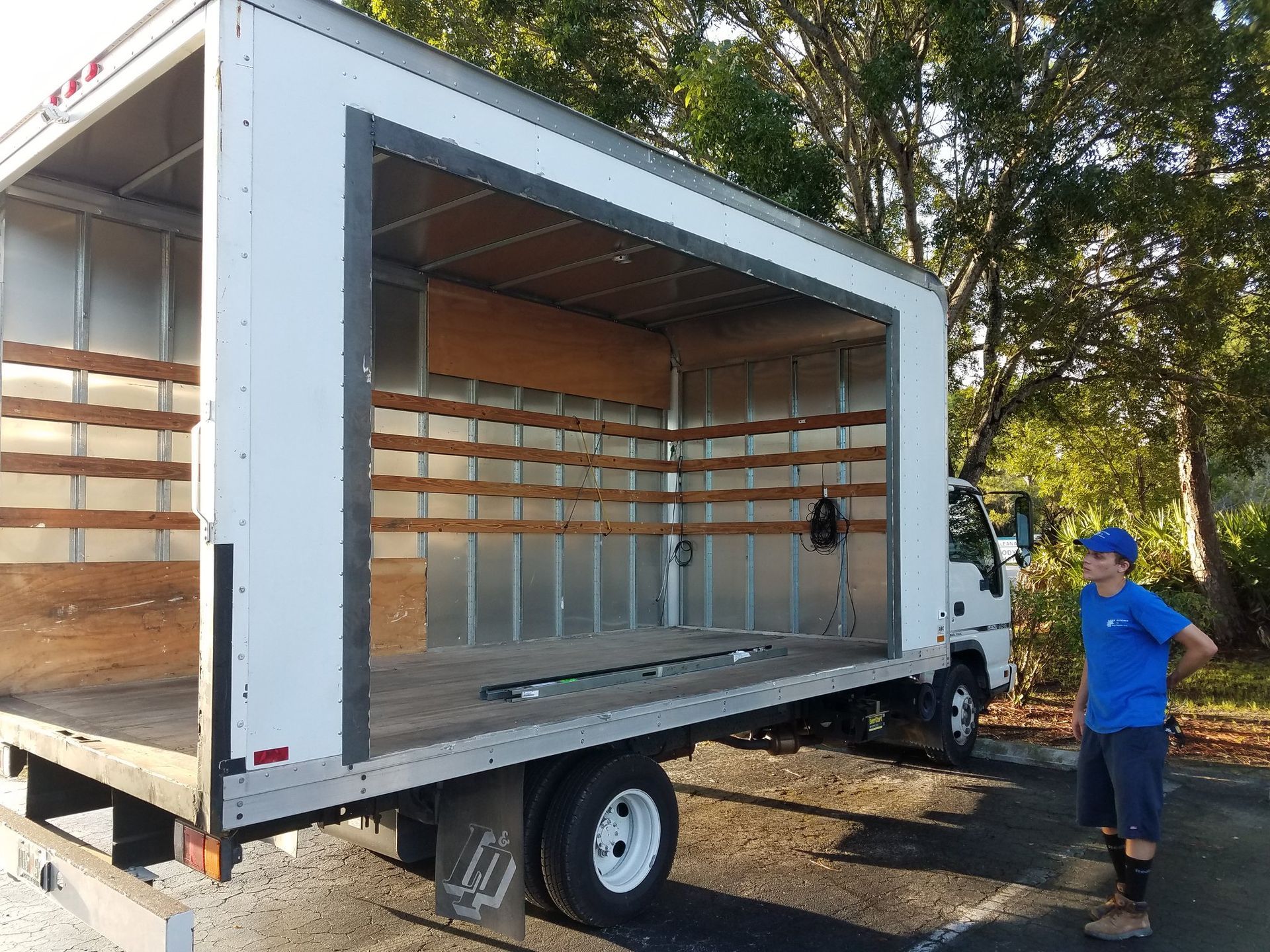 A person stands near an open box truck. The truck is empty inside, and the setting is outdoors.