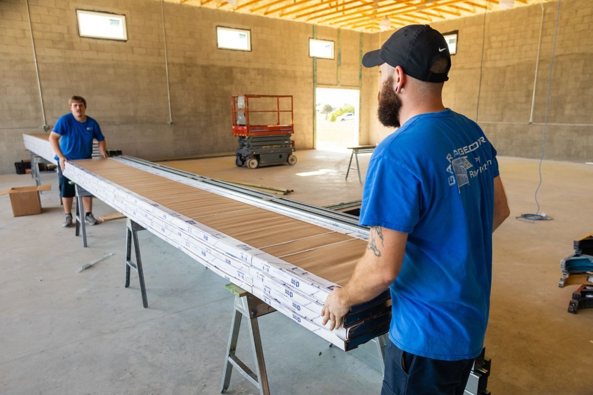 Two men in blue shirts carrying building materials inside a large, unfinished space.