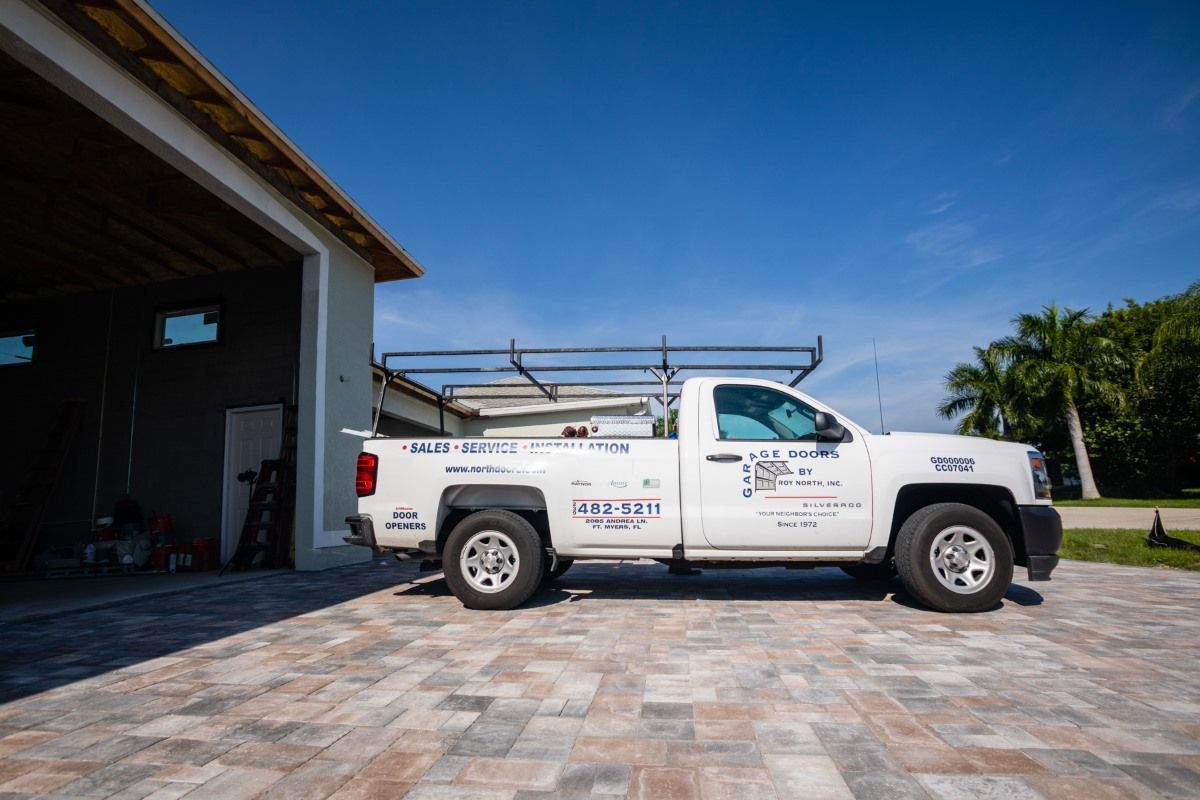 White pickup truck parked on brick driveway near a garage. Truck has a roof rack and company logos.
