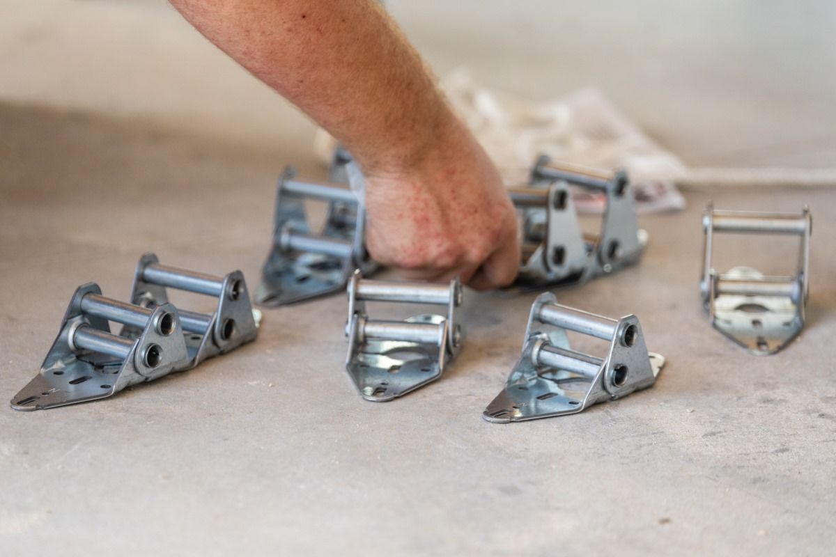Hand arranging several metal garage door hinges on a concrete surface.