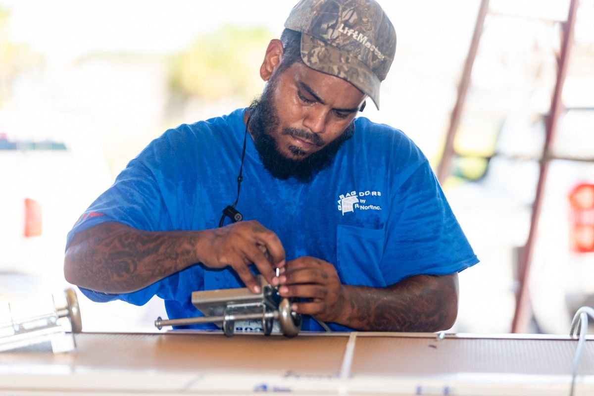 Man in blue shirt and camo hat repairing a machine outdoors.
