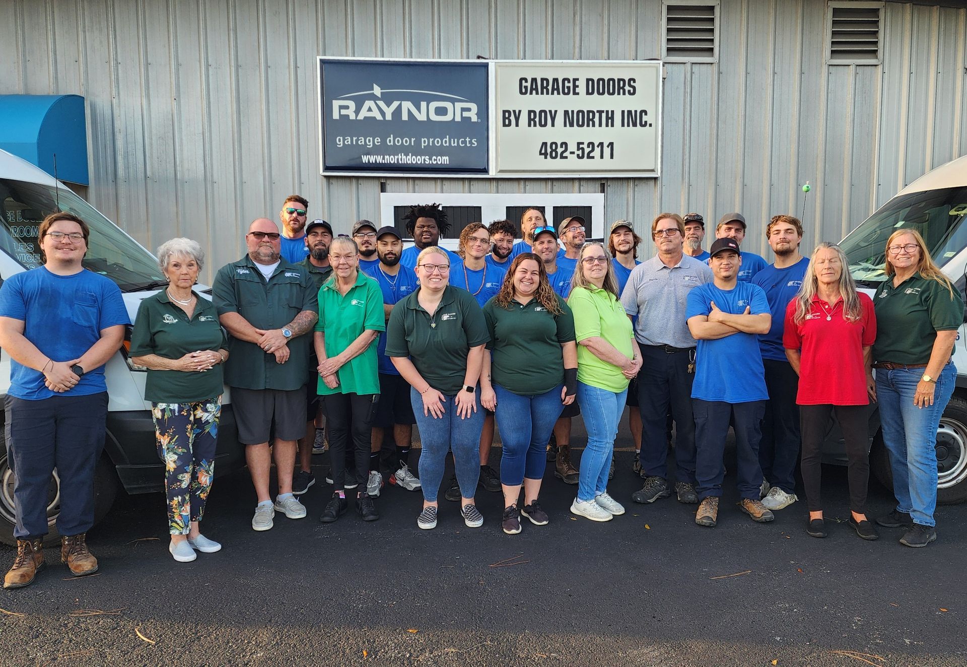 Group photo of Raynor Garage Doors employees outside a building with two vans, wearing various colored shirts.